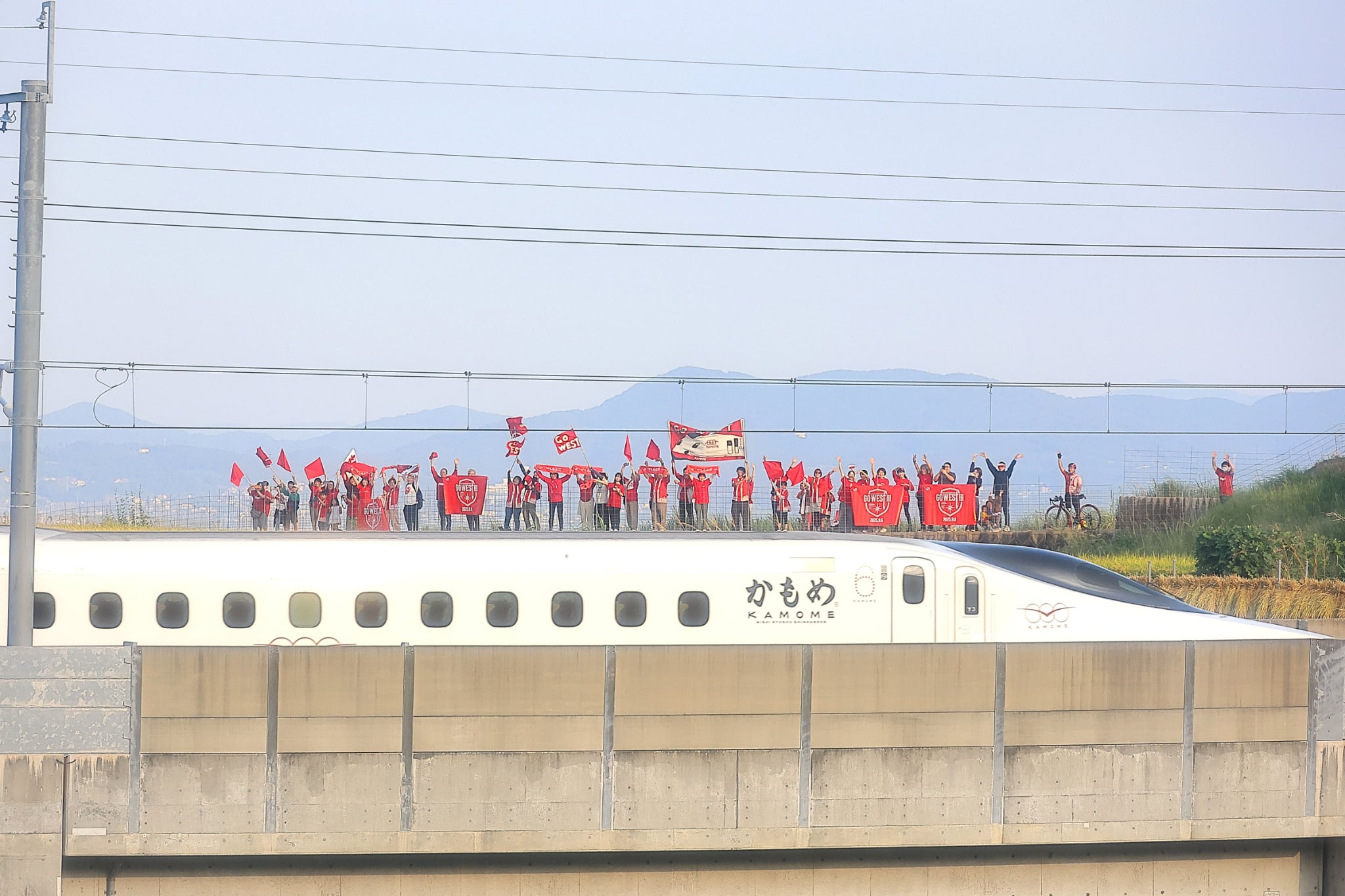 西九州新幹線かもめと、線路沿いで手を振る参加者たち